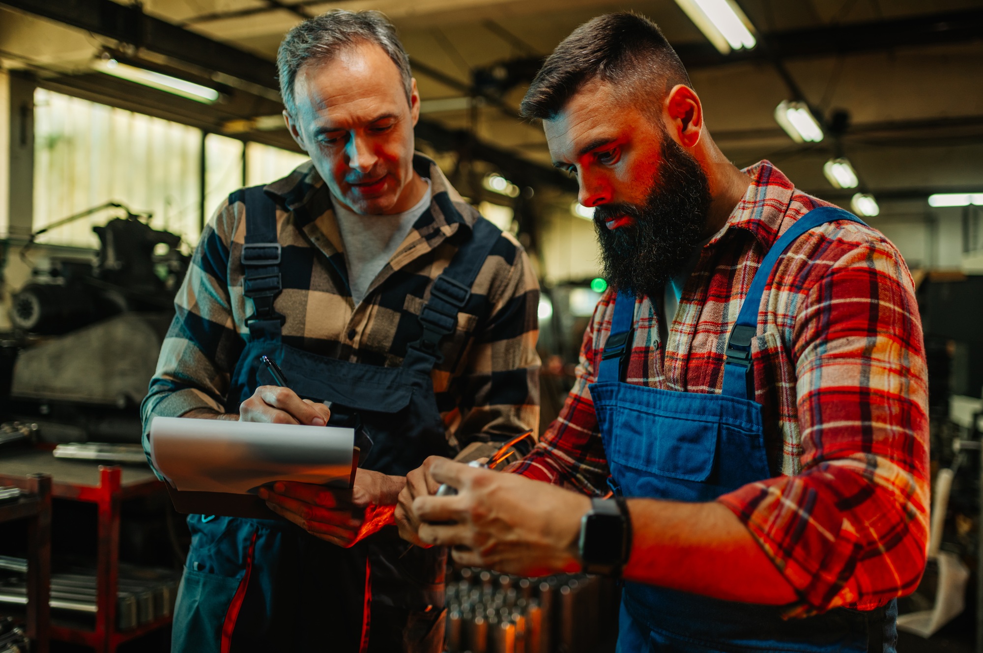 Two metal worker machinist examining a metal object and taking notes.